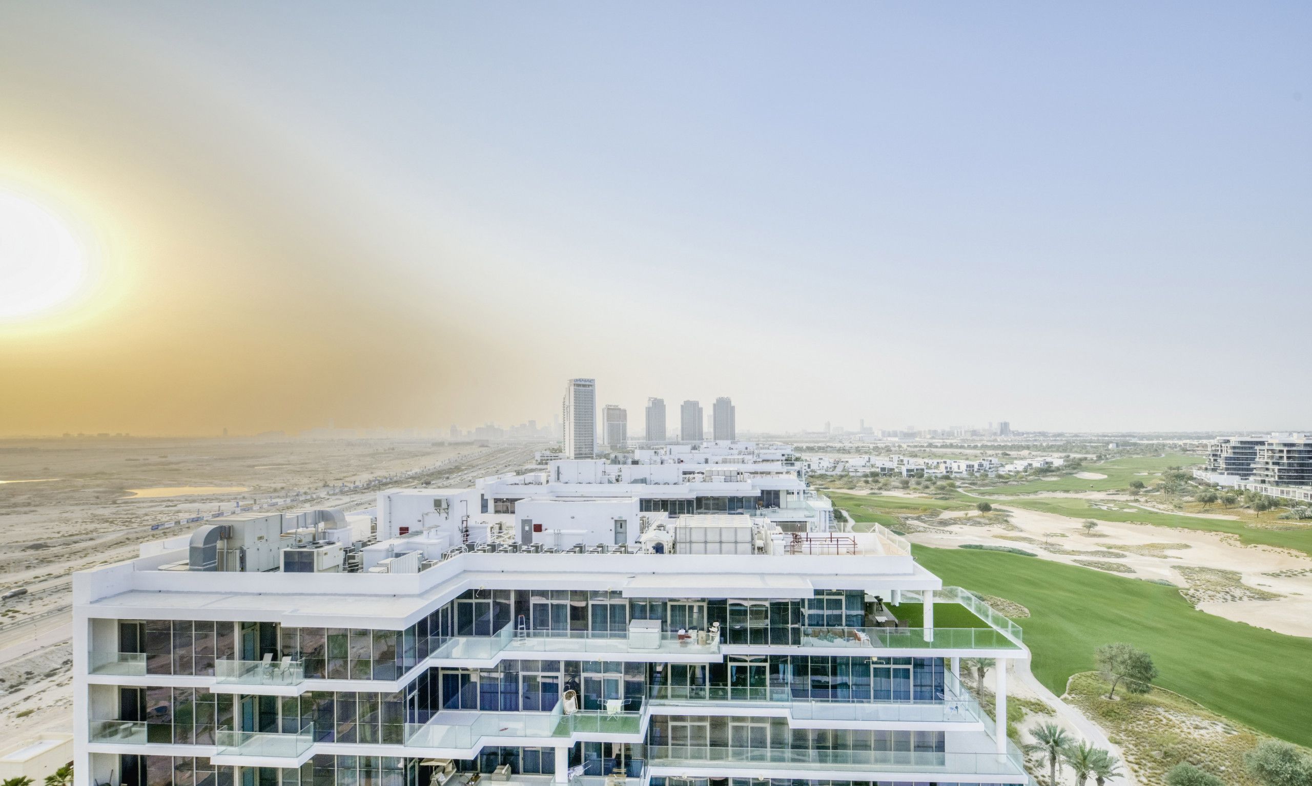 A modern multi-story hotel with a glass facade, located near a golf course and city skyline.