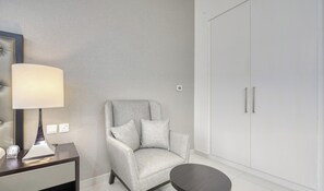 A modern room with a grey upholstered armchair, a small round table, a lamp, and a wardrobe.