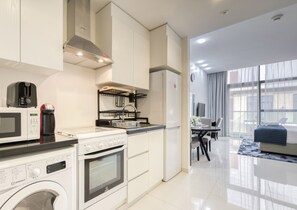 Una cocina moderna con microondas, tostadora, hervidor y lavadora. Cuenta con una zona de comedor con mesa y sillas, y un amplio ventanal que proporciona luz natural.