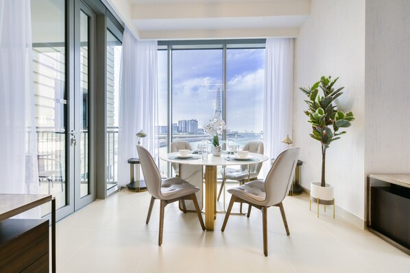 A modern dining area with a round table, four chairs, and a view of the cityscape through large windows.