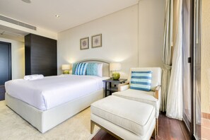 Quarto de hotel com uma cama grande, uma cadeira, uma mesa de cabeceira e uma janela com cortinas.