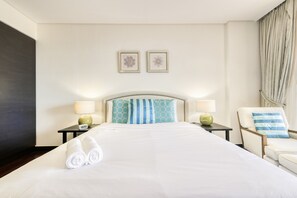 A hotel room with a large bed, two bedside tables with lamps, a chair with a pillow, and two wall-mounted picture frames. - Relaxing 1BR at Anantara North Residences Palm Jumeirah by Deluxe Holiday Homes (Dubai)