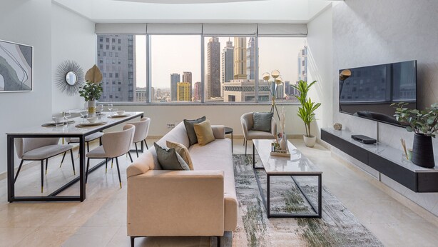 A modern living room with a city view, a dining area, and a TV mounted on the wall.