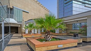 A modern building with a courtyard featuring planters with palm trees and a glass staircase.