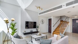 A modern living room with a sofa, coffee table, and a TV. There is a staircase leading to another level.
