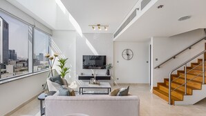 A modern living room with a sofa, coffee table, and TV, a staircase, and a city view.