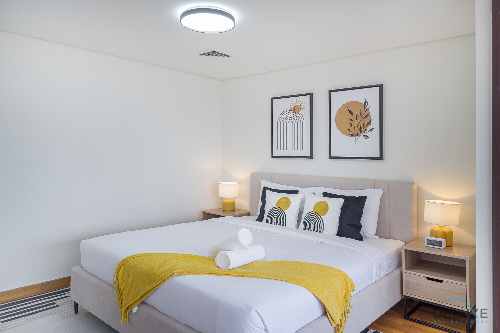 A neatly arranged hotel room with a large bed, two bedside tables with lamps, and two framed artworks on the wall.