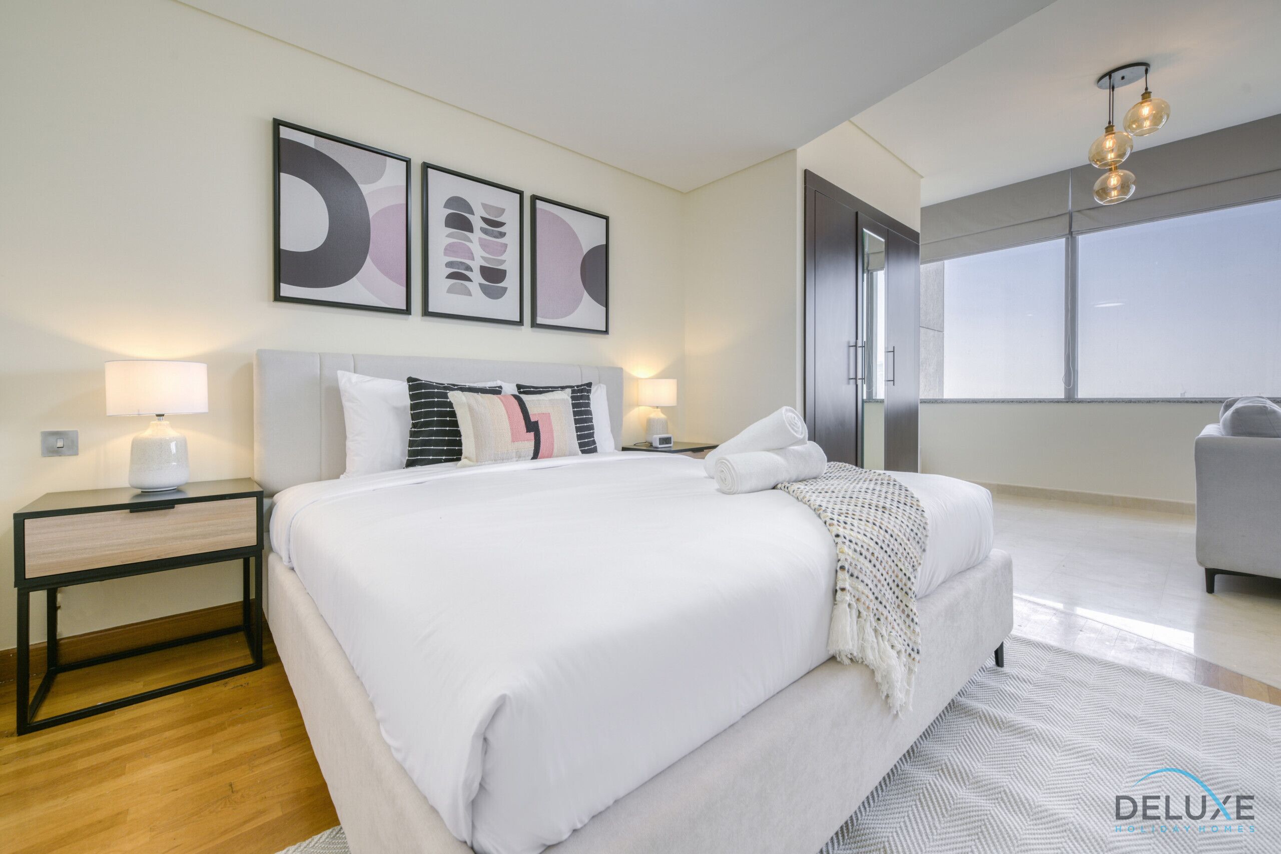 Quarto de hotel moderno com uma cama grande, duas mesas de cabeceira, uma escrivaninha e vista da cidade através de amplas janelas.