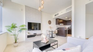 Una sala moderna con una televisión de pantalla plana, una mesa de centro y un sofá. Hay una zona de cocina con una mesa de comedor y sillas.