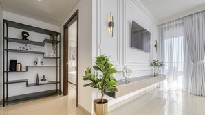 Un salon moderne avec une étagère en métal noir, une plante en pot, un téléviseur à écran plat fixé au mur et une grande fenêtre ornée de rideaux légers.