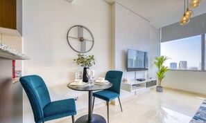 A modern living room with a round dining table, two teal chairs, a TV, and a city view through large windows. - Welcoming Studio at Sky Gardens DIFC by Deluxe Holiday Homes (Dubai)
