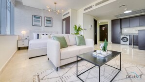 Habitación de hotel moderna con cama, sofá, mesa de centro y zona de cocina con lavadora.