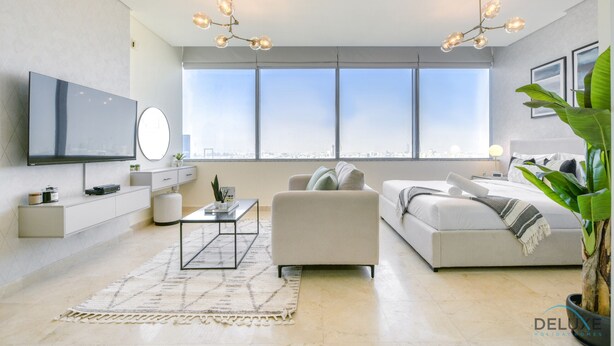 Una sala de estar moderna con un televisor grande, un sofá, una mesa de centro y un ventanal con vista a la ciudad.