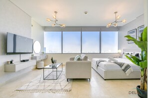 Una sala de estar moderna con un televisor grande, un sofá, una mesa de centro y un ventanal con vista a la ciudad.