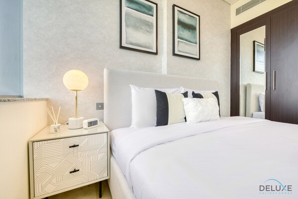 Habitación de hotel con una cama grande, una mesita de noche con lámpara, un reloj digital y cuadros en la pared.