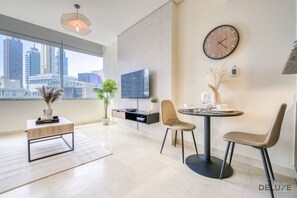 A modern living room with a city view, a flat-screen TV, a round dining table with chairs, and a coffee table.