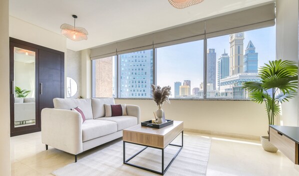 A modern living room with a sofa, coffee table, and large windows offering a city view.