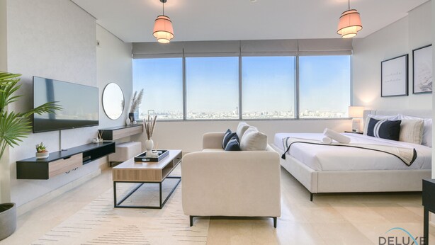 Un soggiorno moderno con una grande TV, un divano, un letto e vista sulla città attraverso ampie finestre.