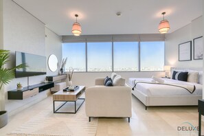 A modern living room with a large TV, a sofa, a bed, and a city view through large windows.