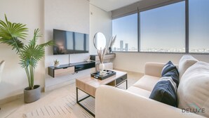 Un soggiorno moderno con una TV a schermo piatto, un tavolino da caffè, un divano e un'ampia finestra con vista sulla città.
