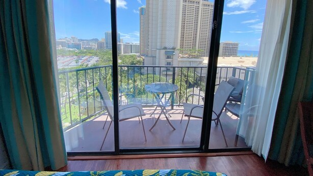 A balcony with a glass door, offering a view of a cityscape and a beach.