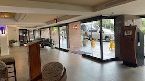 A hotel lobby with a reception desk, seating area, and large glass doors leading outside.