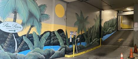 A parking garage with a mural of palm trees and a sun, and a sign indicating 'Palms Parking 1850 Ala Moana.'