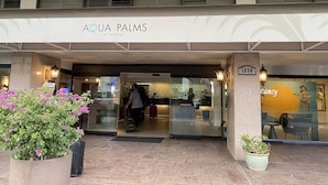The entrance to Aqua Palms at Waikiki, featuring a modern facade, glass doors, and a sign indicating the address.