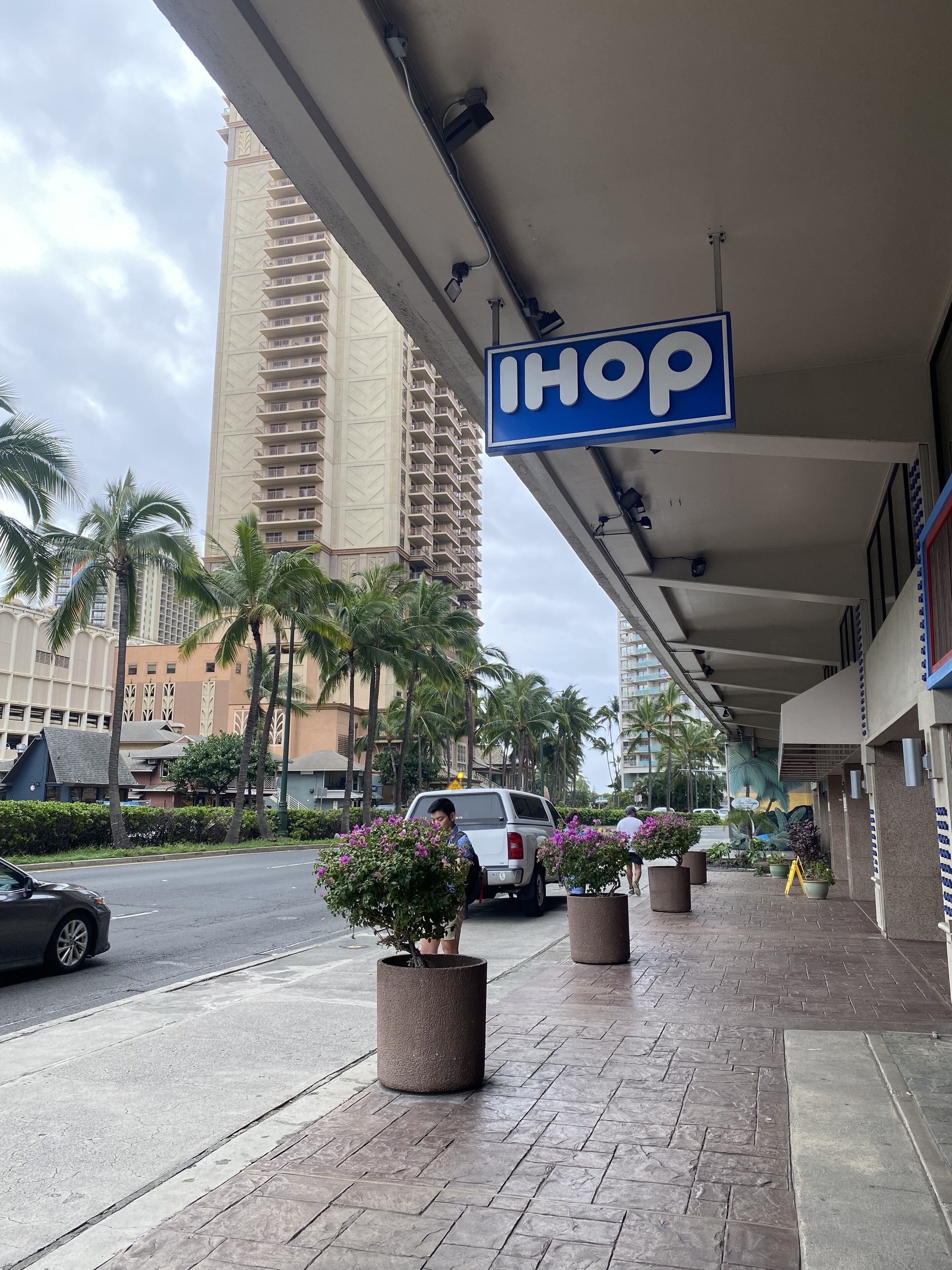 A hotel entrance with a sign reading "IHOP" and a parking area with a white SUV.