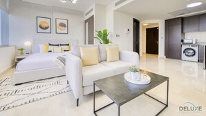 Una habitación de hotel moderna con cama, sofá, mesa de centro y una zona de cocina con lavadora.