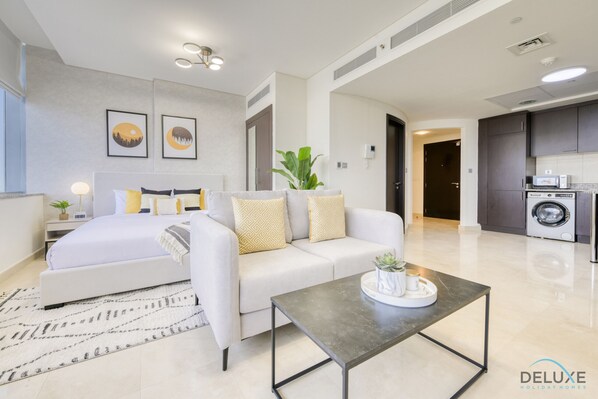A modern hotel room with a bed, sofa, coffee table, and a kitchen area with a washing machine.