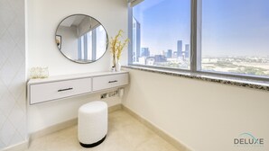 Un baño moderno con un ventanal grande, un espejo redondo, un tocador blanco y un taburete pequeño.