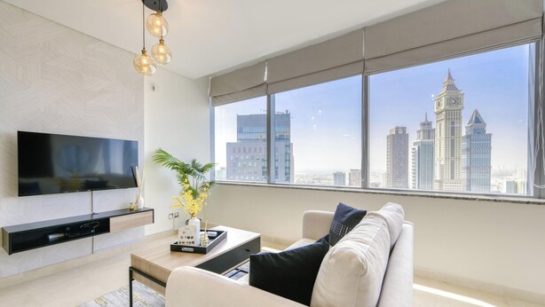 Una sala de estar moderna con una televisión de pantalla plana, una mesa de centro, un sofá y un amplio ventanal con vistas a la ciudad.