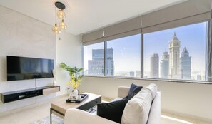 Uma sala de estar moderna com televisão de tela plana, mesa de centro, sofá e uma janela grande com vista para a cidade.
