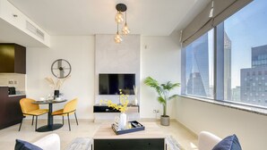 Una sala de estar moderna con sofá, mesa de centro y comedor con sillas. Hay un televisor montado en la pared y un ventanal con vistas a la ciudad.