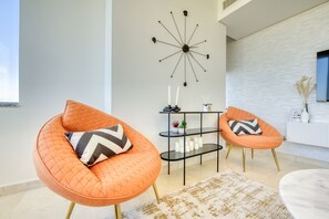 A modern living room with two orange armchairs, a black side table with candles, and a decorative wall clock.