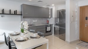 A modern kitchen with grey cabinets, a stainless steel refrigerator, and a dining area with a white table set for four. - Scenic 1BR at Ocean Heights Dubai Marina by Deluxe Holiday Homes (Dubai)