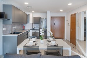 A modern kitchen with grey cabinets, a stainless steel refrigerator, and a dining area set for four with white tableware.