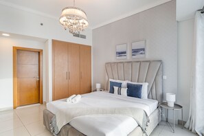 A modern bedroom with a large bed, a wooden wardrobe, a chandelier, and two framed pictures on the wall.