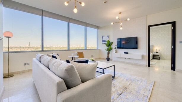 Uma sala de estar moderna com uma janela grande, um sofá, uma mesa de centro e uma TV fixada na parede.