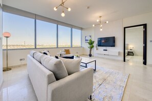 A modern living room with a large window, a sofa, a coffee table, and a TV mounted on the wall.