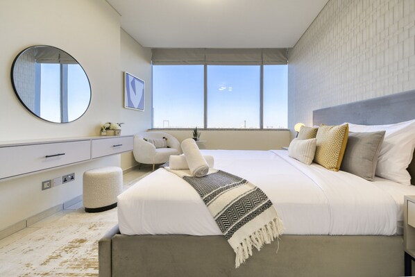 A modern bedroom with a large bed, a round mirror, a view of the city, and a minimalist design.
