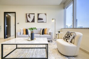 Uma sala de estar moderna com sofá, poltrona e mesa de centro. Há obras de arte abstratas nas paredes e vista da cidade por grandes janelas.