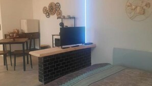 Une pièce de taille modeste comprenant un lit, un petit bureau avec une télévision et une étagère fixée au mur.