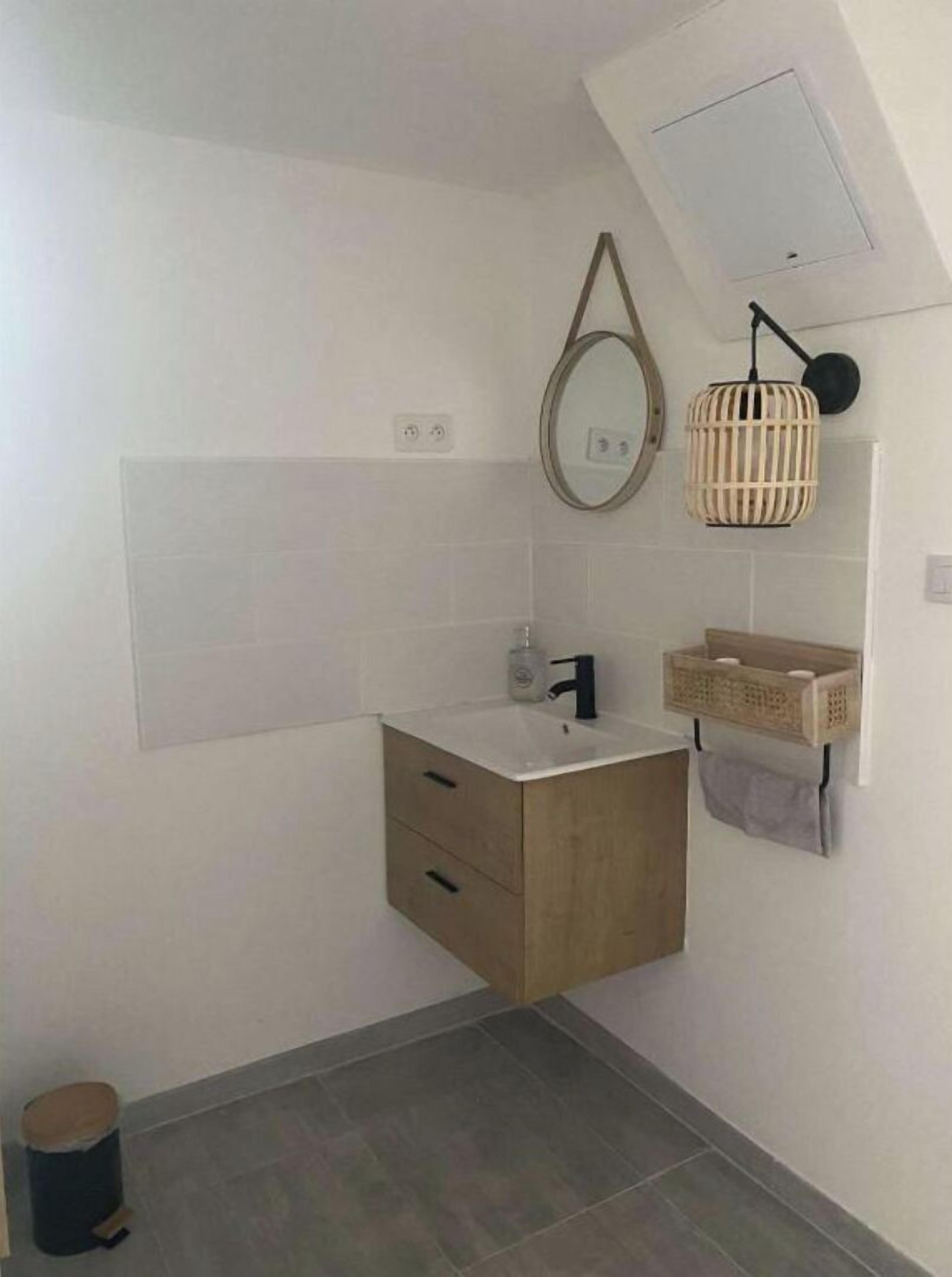 Ein Badezimmer mit Waschtisch aus Holz, einem Spiegel, einem Handtuchhalter und einer kleinen Mülltonne.