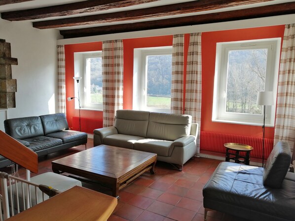 A living room with a sofa, armchair, and coffee table. There are two windows with curtains, a radiator, and a lamp. - Le clos Charmarin, between city center and countryside (Besançon)