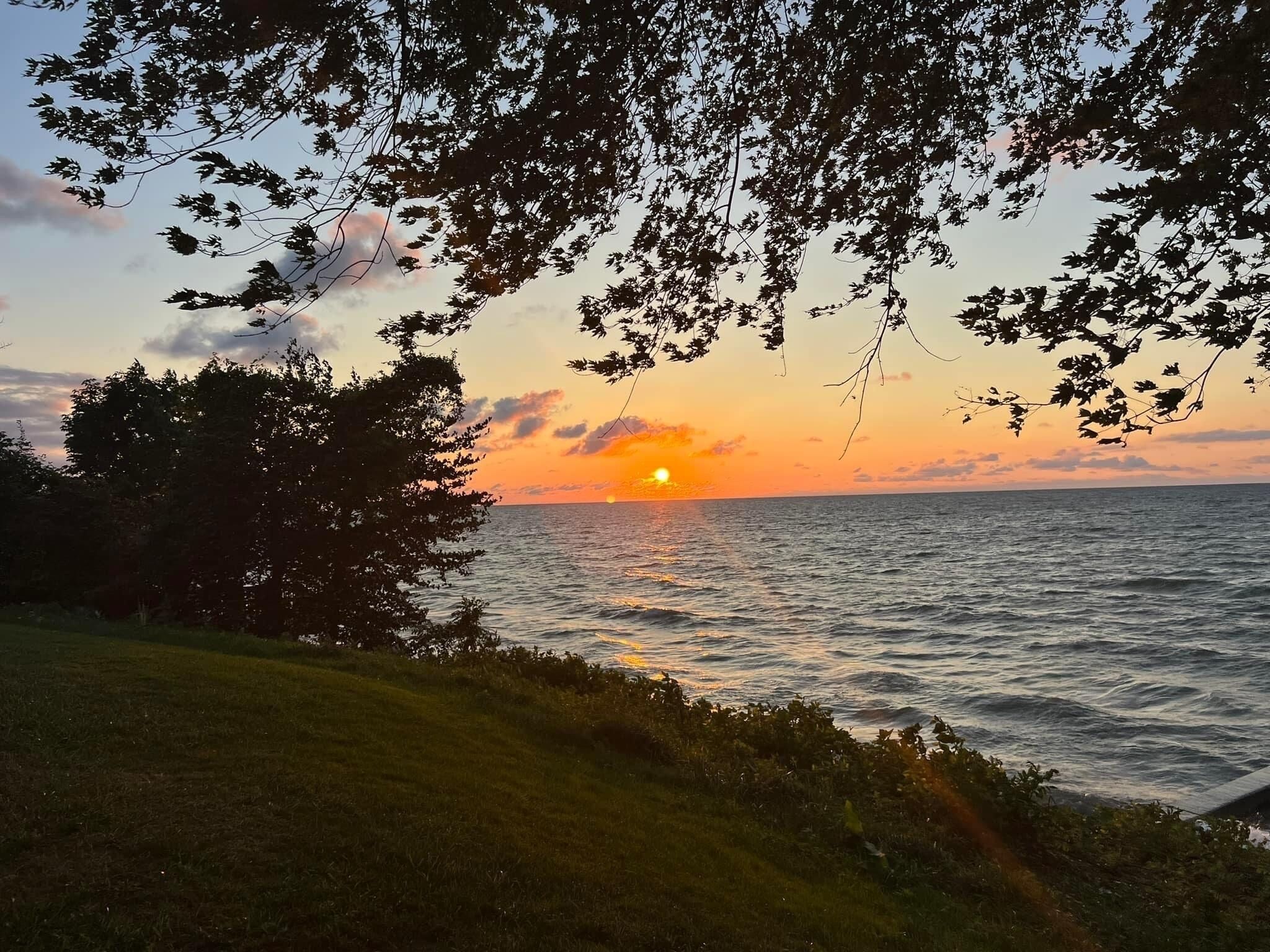 Un coucher de soleil sur une étendue d’eau, avec des arbres encadrant le paysage.