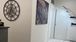 Un couloir avec un sol en marbre, une horloge murale, un tableau et une porte.