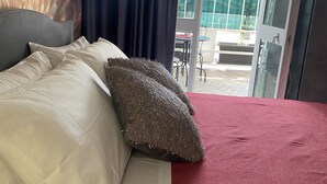 Un lit avec des oreillers blancs et gris, une couvre-lit rouge et un coussin à texture.