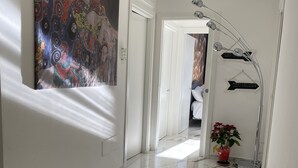 Un couloir doté d’un sol en marbre, une grande peinture abstraite sur le mur de gauche et une plante dans un pot rouge sur le mur de droite.